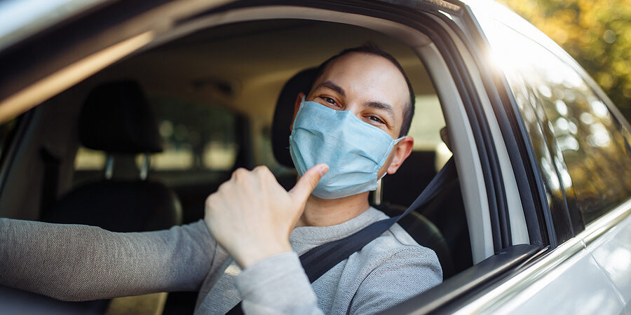 A man drives a car wearing medical mask during coronavirus outbreak. Taxi driver delivers his passanger to the destination. Social distance, new normal, virus spread prevention and treat concept